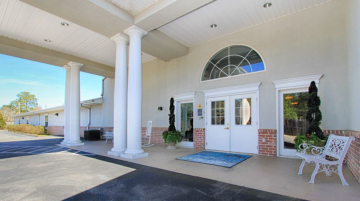 A building entrance featuring white columns and an arched window above double doors.