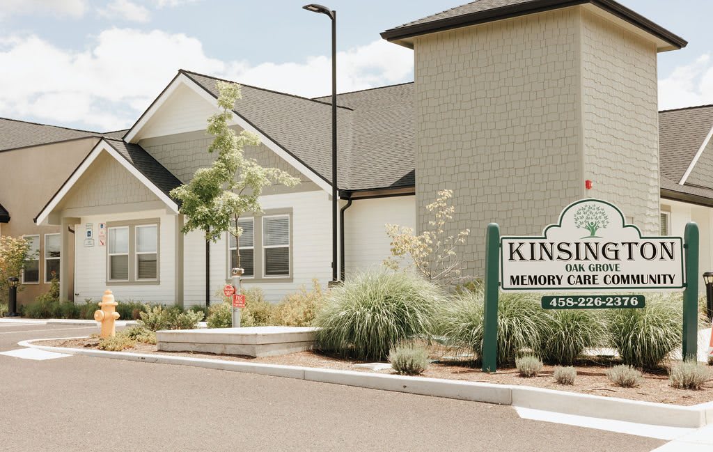 A street view of a modern apartment complex with well-maintained landscaping and an entrance sign.