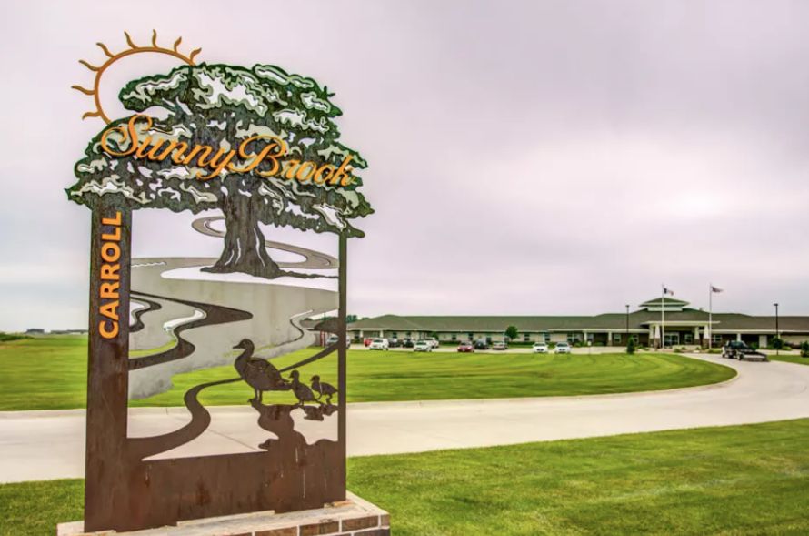 A scenic view of a golf course entrance with a decorative sign and a clubhouse in the background.