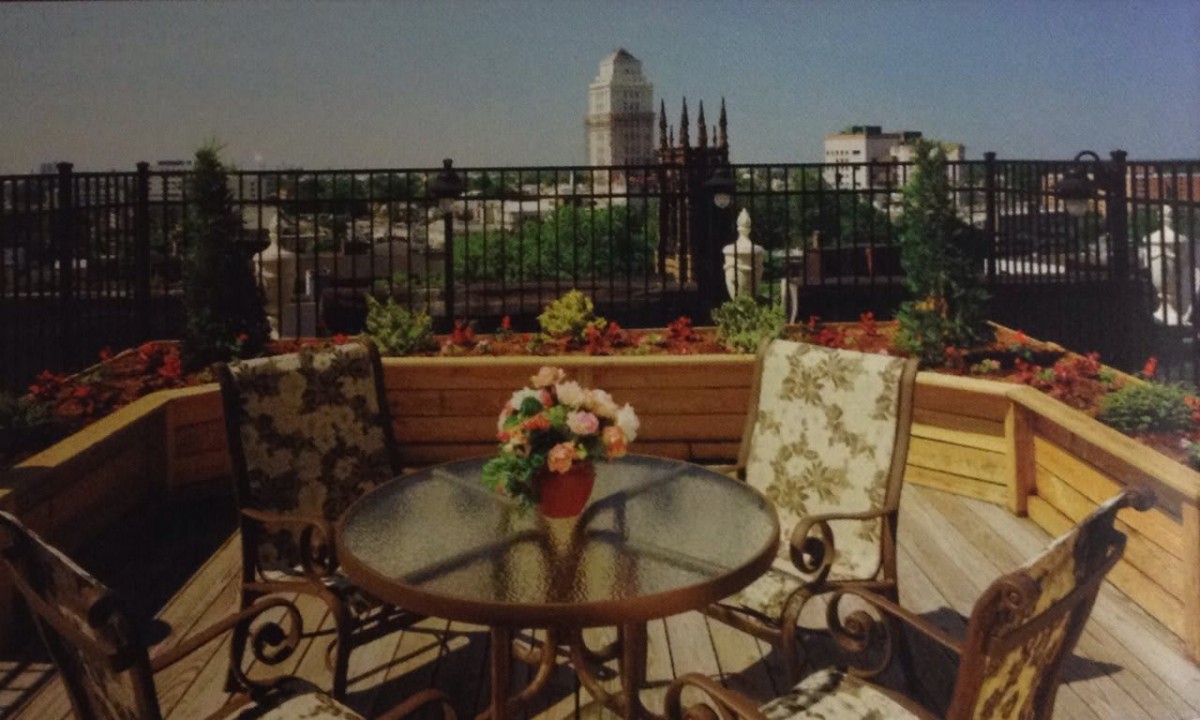 A cozy outdoor patio with a table and chairs overlooking a city skyline on a sunny day.