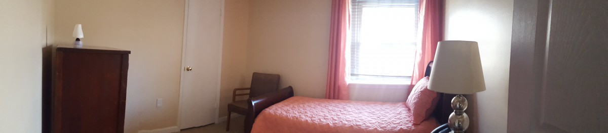 A minimalist bedroom with a bed, chair, and window with pink curtains.