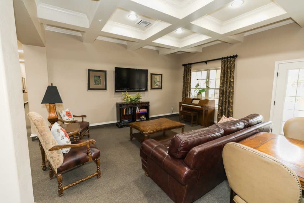 A cozy living room with a leather sofa, armchair, and a large TV mounted on the wall, featuring elegant decor and a coffered ceiling.