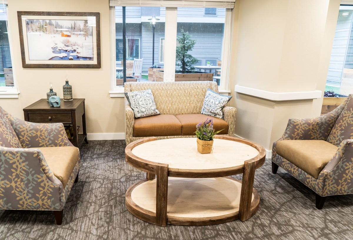 A cozy living room with a sofa, armchairs, and a coffee table, featuring a large window and decorative elements.