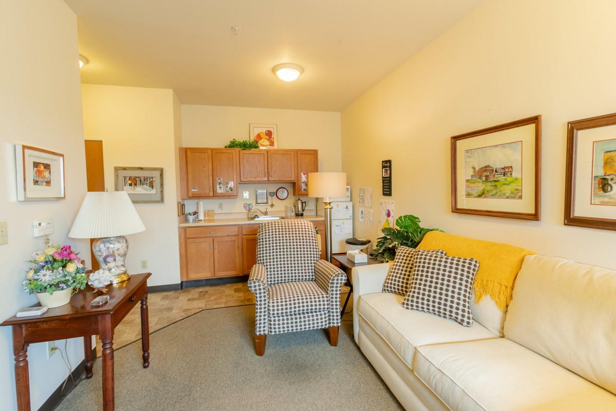 A cozy apartment living room featuring a kitchenette, sofa, and armchair.
