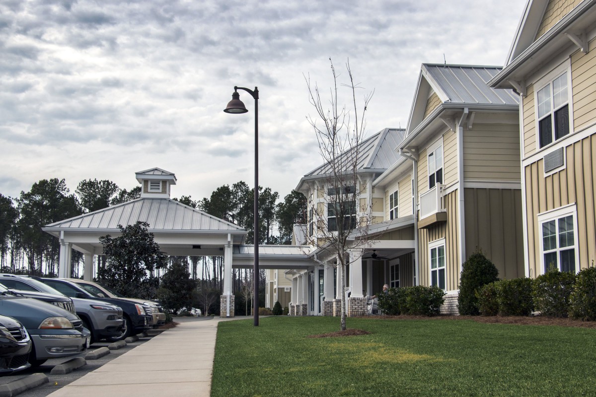 A view of a modern building with a parking lot and sidewalk under an overcast sky.