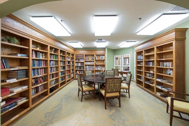 A cozy library room with wooden bookshelves, a round table, and chairs.