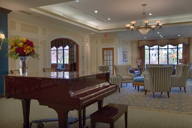 A cozy living room featuring a grand piano and elegant furnishings under a stylish chandelier.