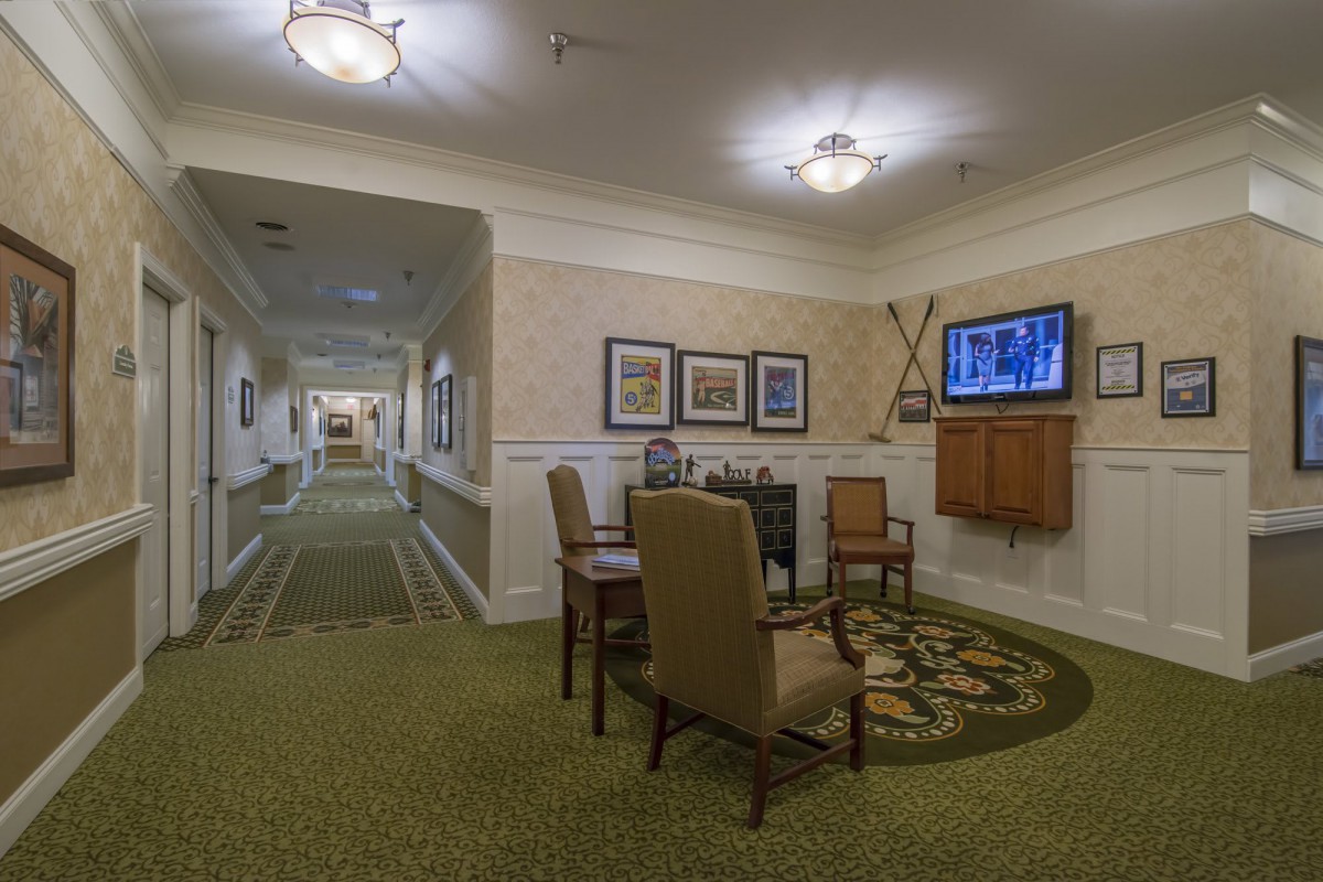 A hallway with a seating area featuring chairs and a table, decorated with paintings and a mounted TV.