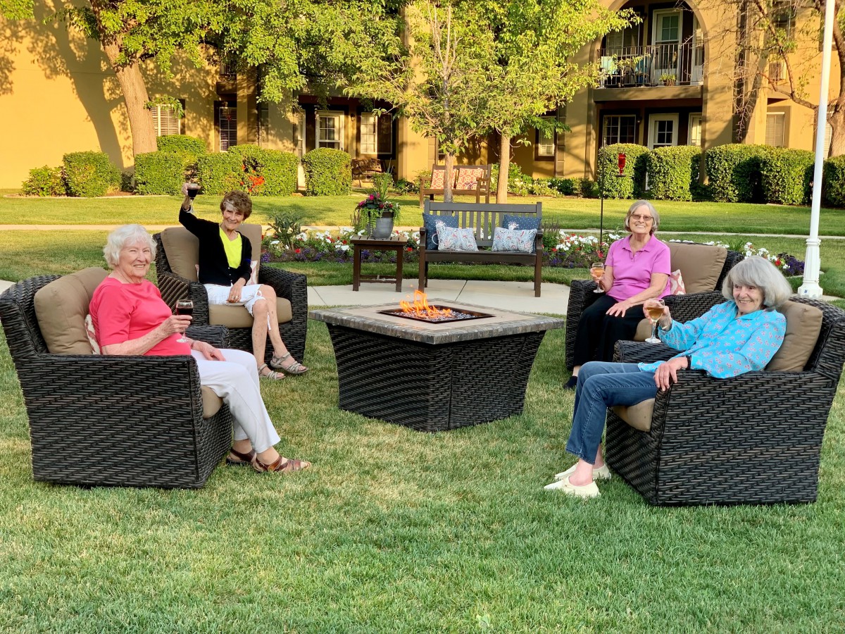 A group of people enjoying an outdoor gathering, sitting around a table on a grassy area.