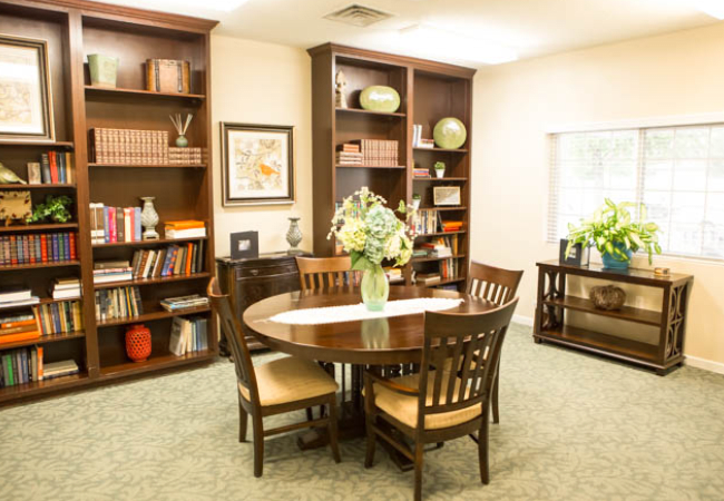 A cozy library interior with bookshelves, a round table, and chairs.