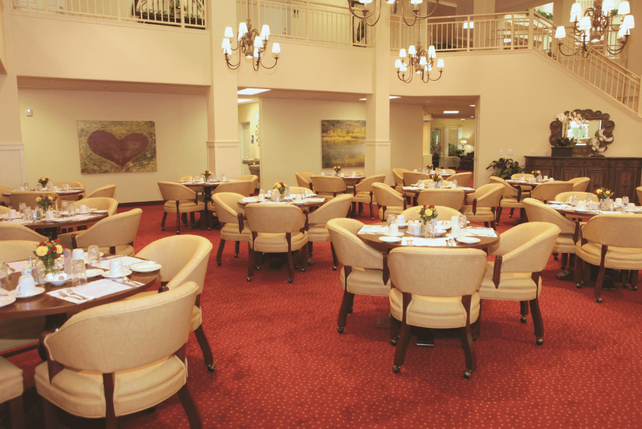 An elegant restaurant interior with round tables, cushioned chairs, and chandeliers.
