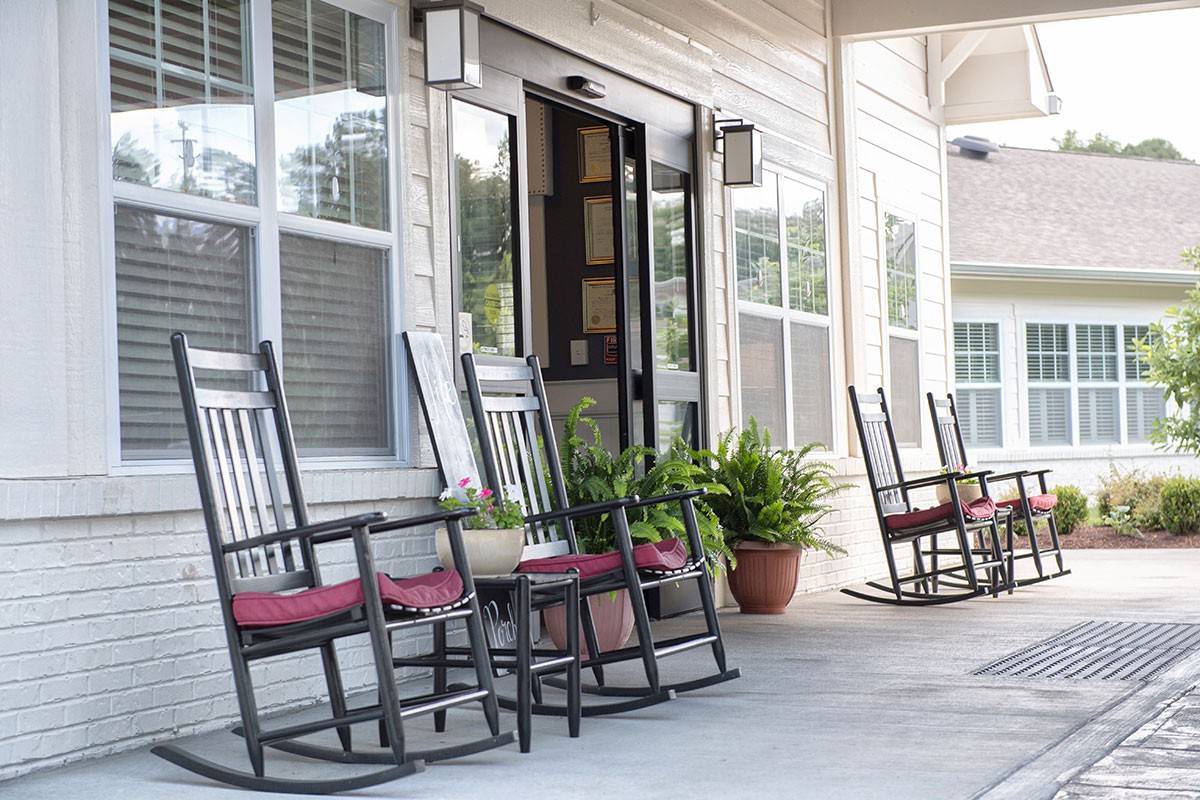 A cozy porch featuring several rocking chairs and potted plants.