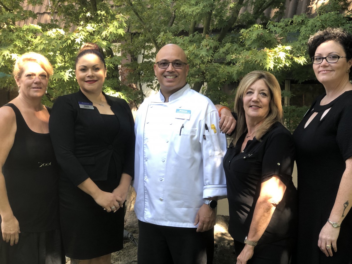 A group of people posing outdoors, including a chef in uniform.