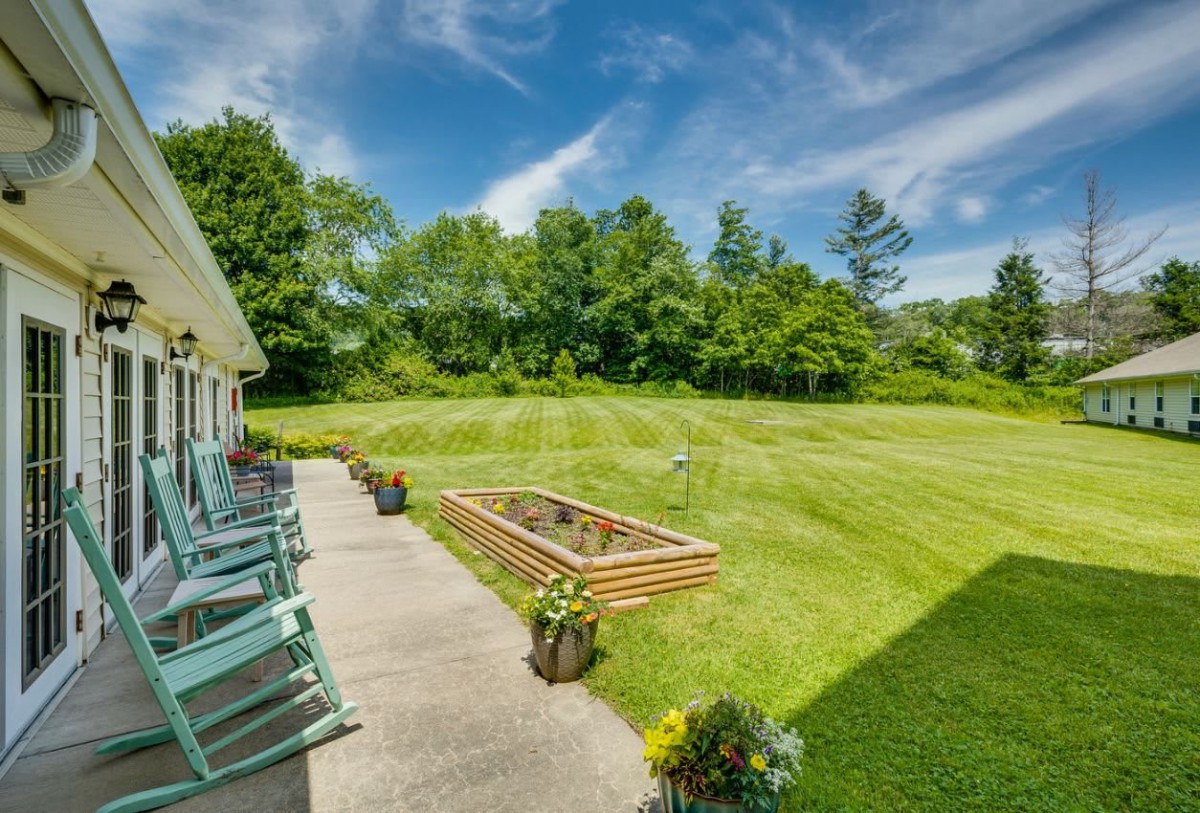 A spacious backyard with a well-maintained lawn, raised garden bed, and patio seating under a clear blue sky.