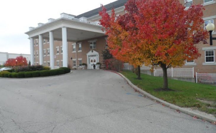 A building entrance with autumn trees displaying vibrant red leaves.