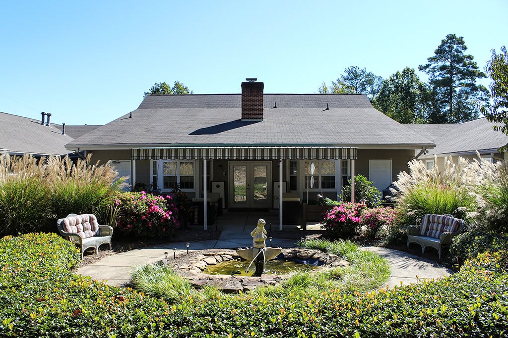 A quaint house with a welcoming garden and fountain in the foreground.