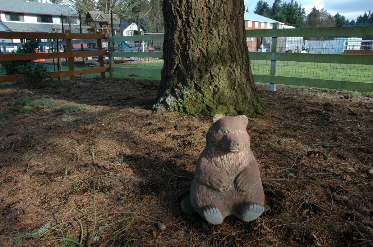 A wooden animal sculpture beneath a large tree in a park setting.