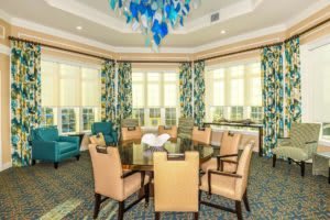 Elegant dining room with a large round table, surrounded by chairs and illuminated by a vibrant chandelier.