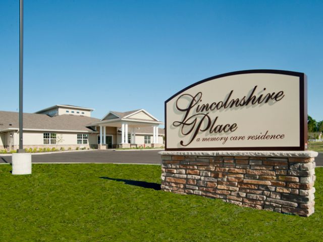 A view of Lincolnshire Place, a retirement home residence, with a prominent sign and manicured lawn on a sunny day.