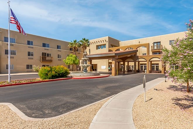 A modern hotel entrance with palm trees, set in a desert-like landscape.