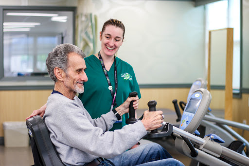 A caregiver assists an elderly man with his exercise routine, promoting rehabilitation and wellness.