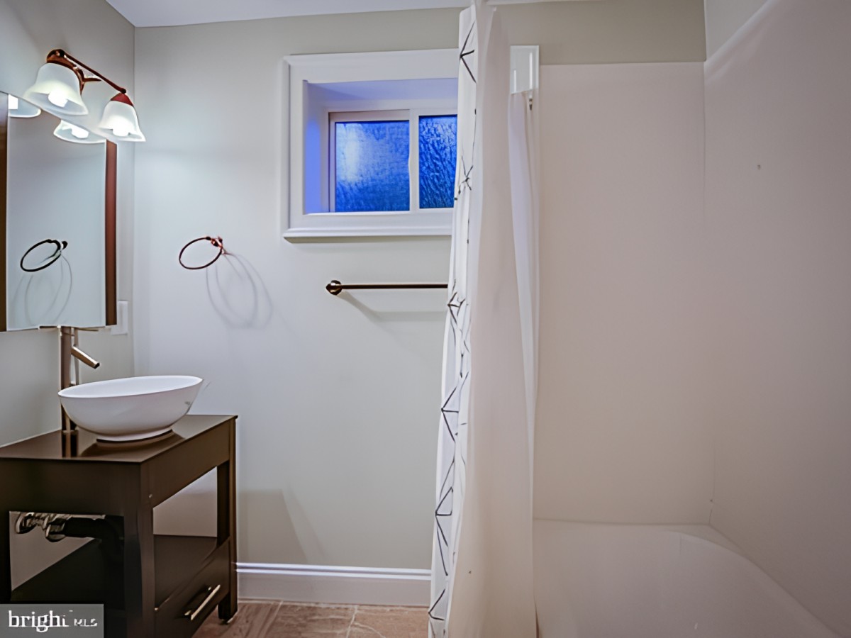 A modern bathroom with a shower, sink, and window.