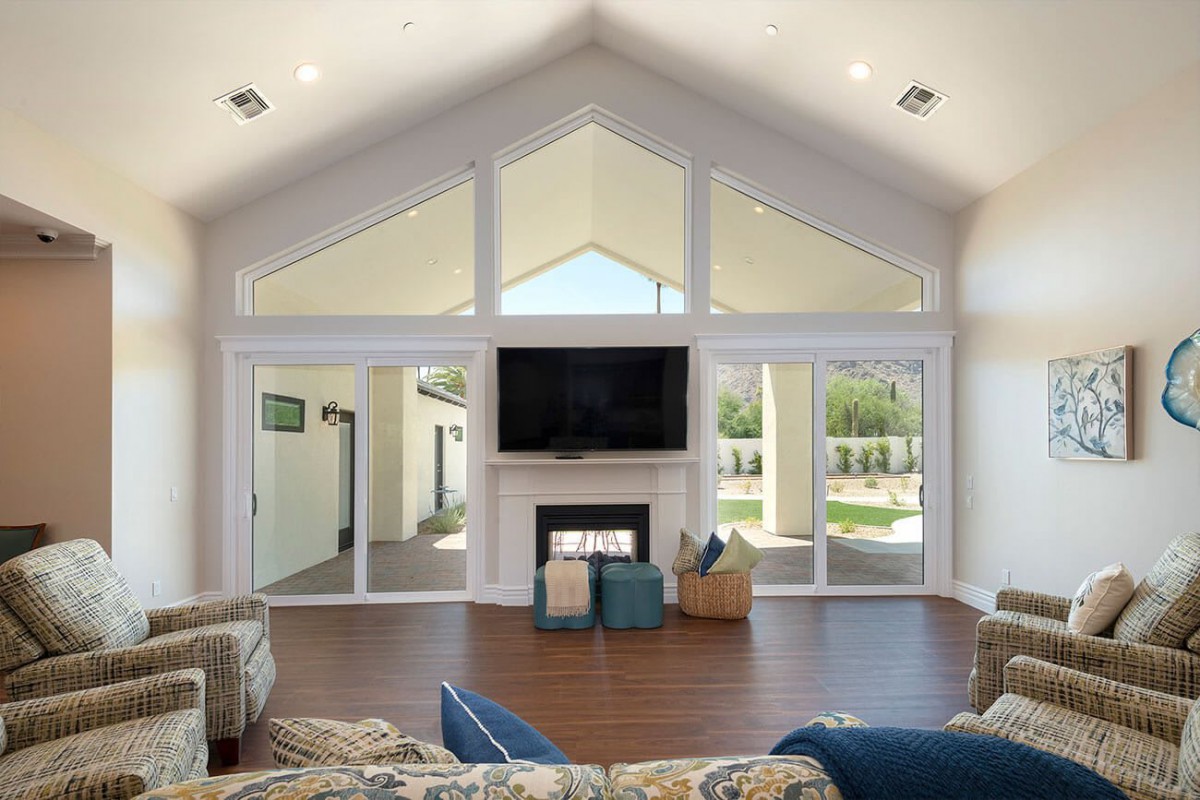 A spacious living room with a vaulted ceiling and large windows, featuring a central fireplace and television.