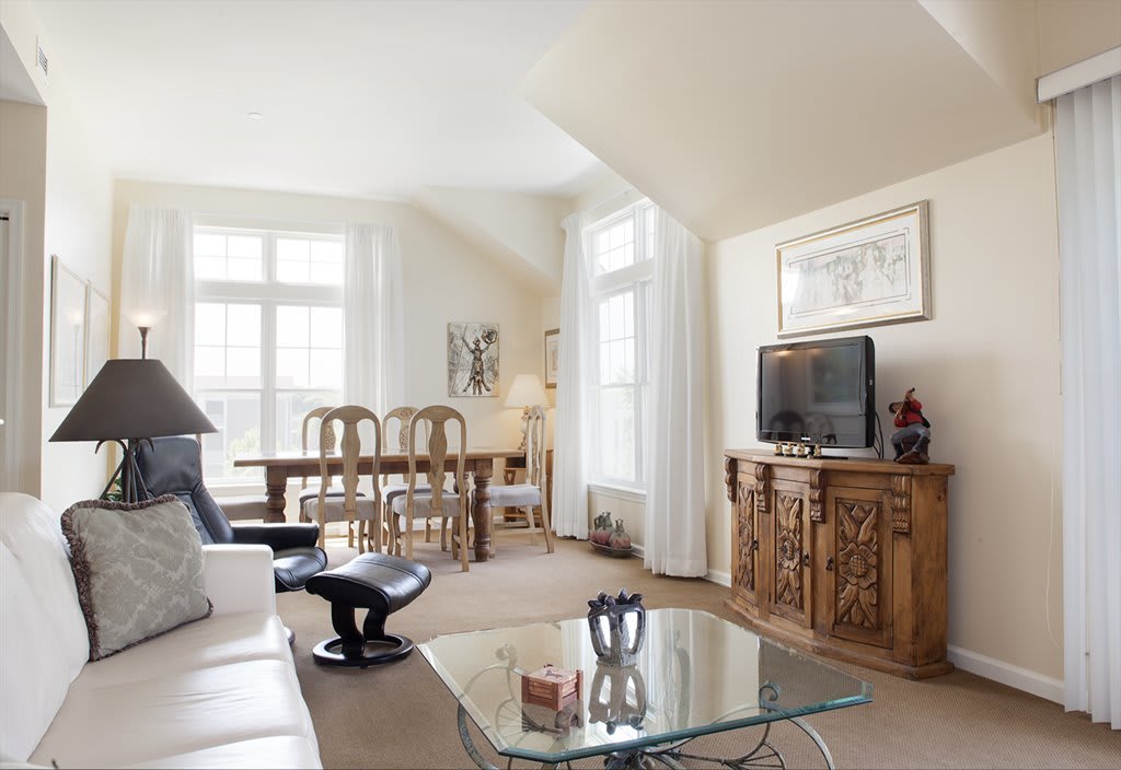 A bright and spacious living room with a dining area, featuring wooden furniture and a glass coffee table.