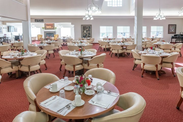 A spacious dining area with neatly arranged tables and chairs on a red carpet.