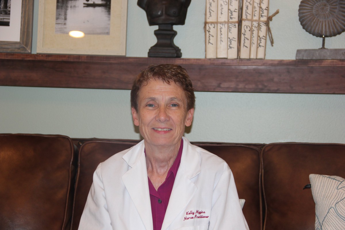 A woman sitting indoors wearing a white coat.