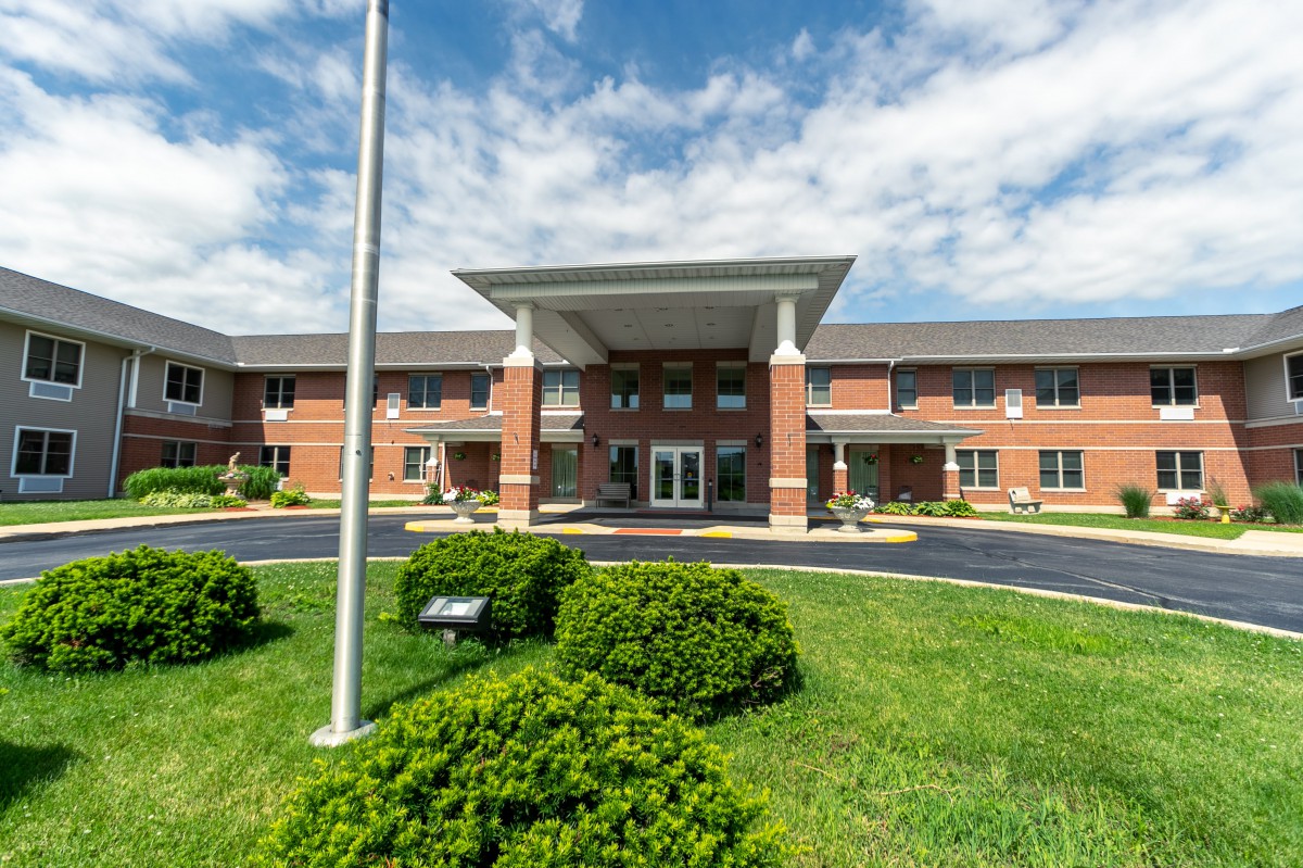 A two-story brick building with a landscaped entrance and flagpole under a cloudy sky.