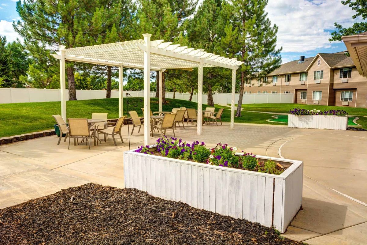 A scenic outdoor patio with a pergola, seating area, and planter box filled with flowers.