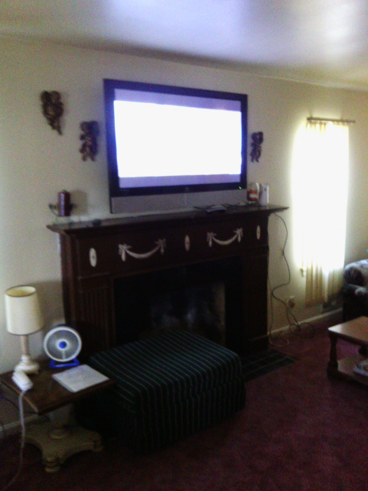 A cozy living room featuring a TV mounted above a fireplace with surrounding decor and furniture.