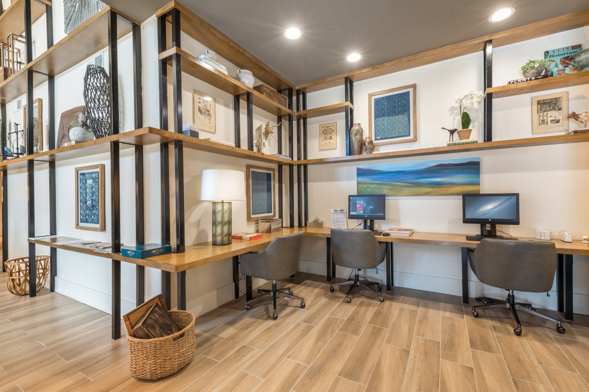 A modern office interior with wooden shelving, two desks equipped with computers, and stylish lighting.