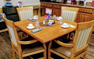 A dining table set for four with neatly arranged tableware and a centerpiece inside a room.