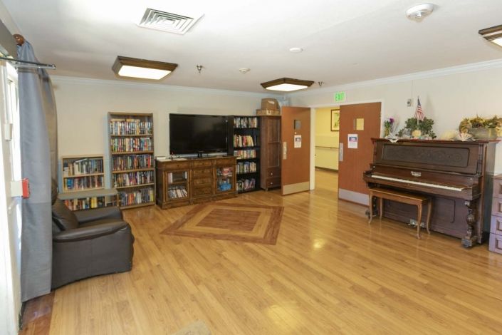 A cozy entertainment room featuring a large television, bookshelves, and a piano.