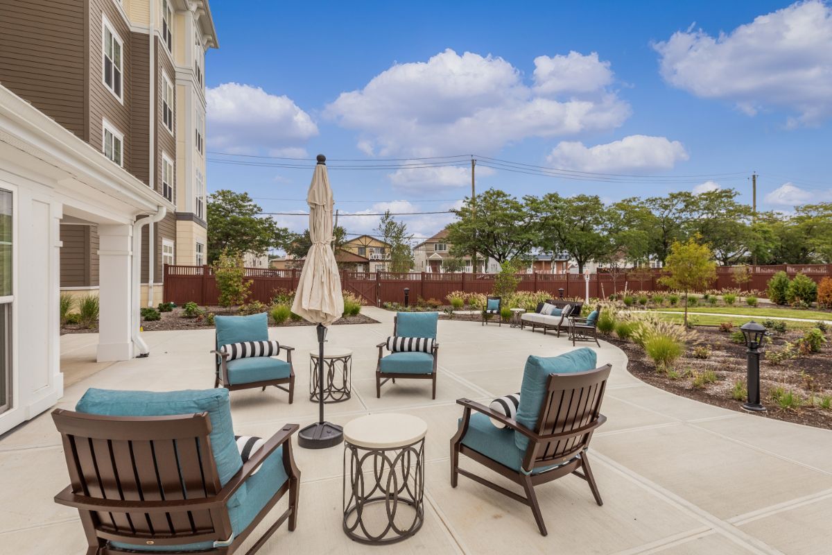 A well-furnished outdoor patio area with chairs and a table under an umbrella, set against landscaped surroundings.