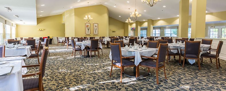 An elegant dining room with neatly set tables and chairs, adorned with chandeliers and decorative artwork.