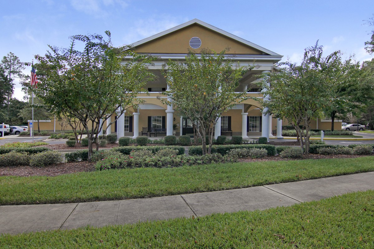 A large, two-story yellow building with columns, surrounded by a well-maintained garden and lawn.
