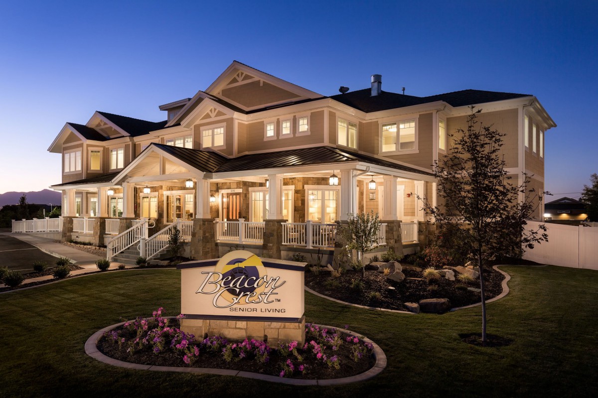 A well-lit residential building at night with a porch and landscaped garden.