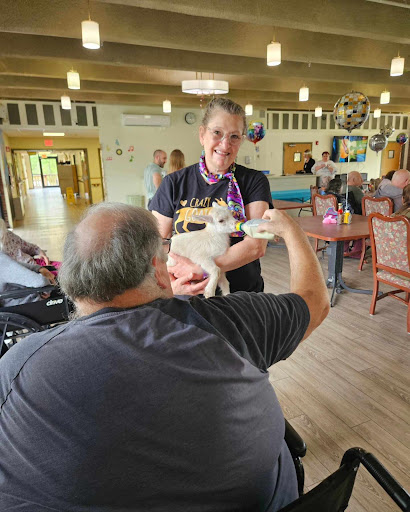 A person holding a small dog while another individual interacts with them in a warm indoor setting.