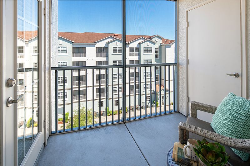 A cozy balcony with seating, overlooking apartment buildings under a clear blue sky.