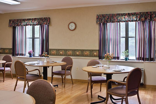 A cozy dining room setup with wooden tables and chairs, featuring large windows adorned with curtains.