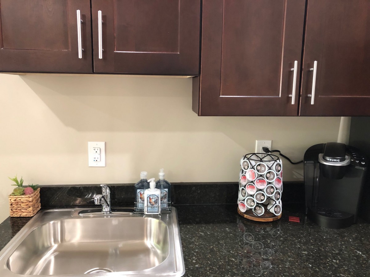 A kitchen countertop with a sink, soap dispenser, coffee maker, and cabinets above.