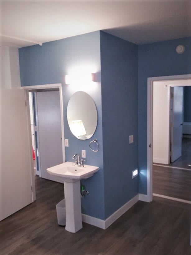 A modern bathroom with blue walls featuring a pedestal sink and a round mirror.