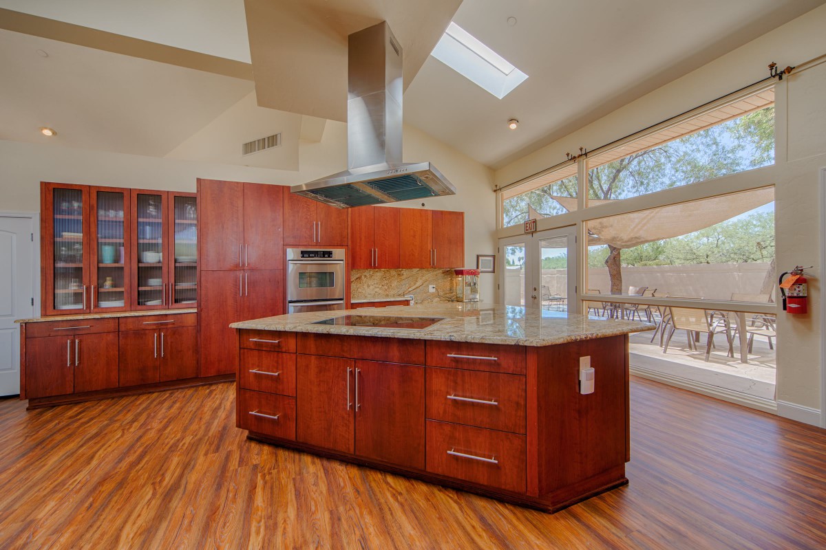 A modern kitchen with an island counter and wooden flooring, featuring stainless steel appliances and abundant natural light.