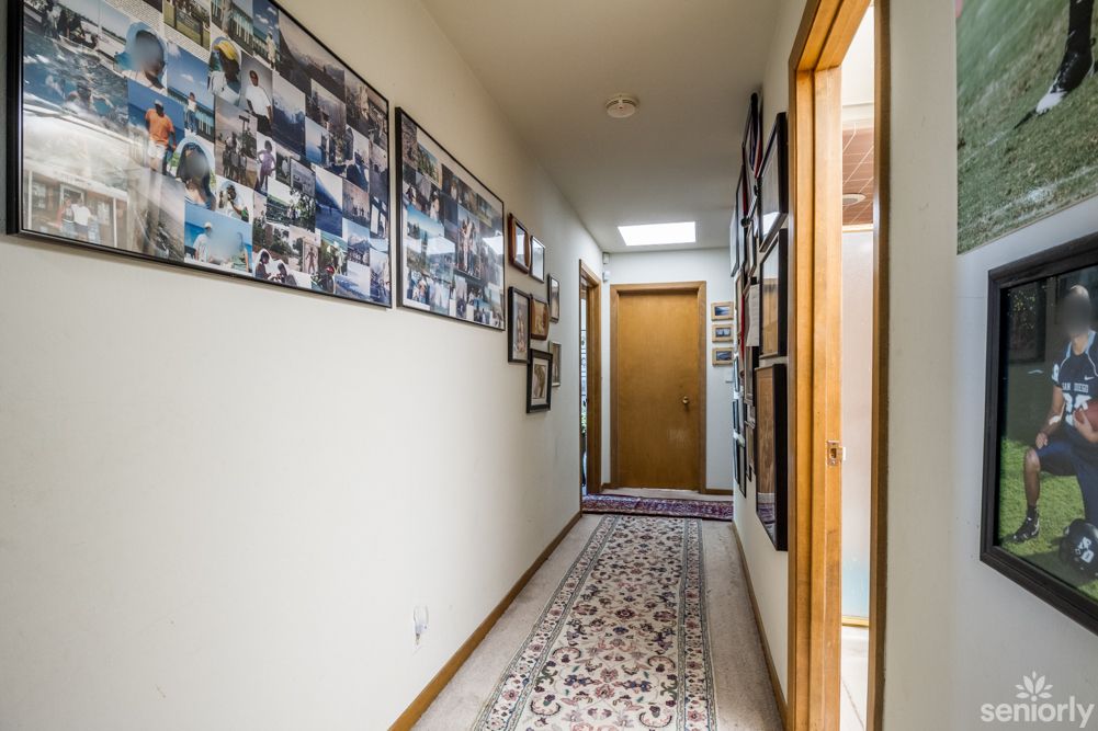 A hallway with photo frames on the wall and a decorative rug leading to a wooden door.