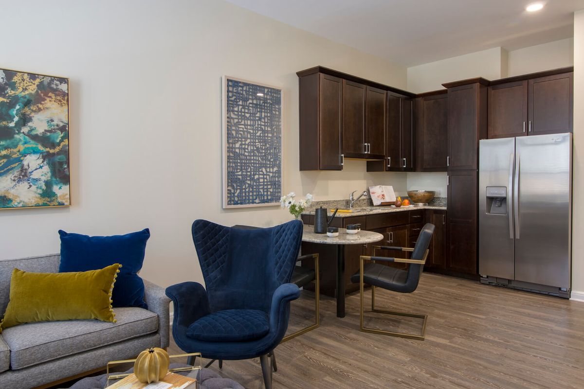 A cozy living and kitchen area featuring modern furniture with a blue armchair and dark wooden cabinets.