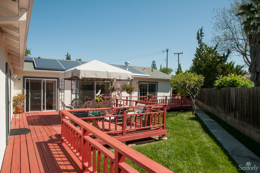 A sunny backyard with a wooden deck, patio furniture, and an umbrella.