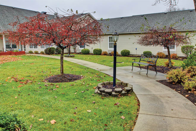 A residential garden scene with autumn trees, a pathway, benches, and a lamp post.